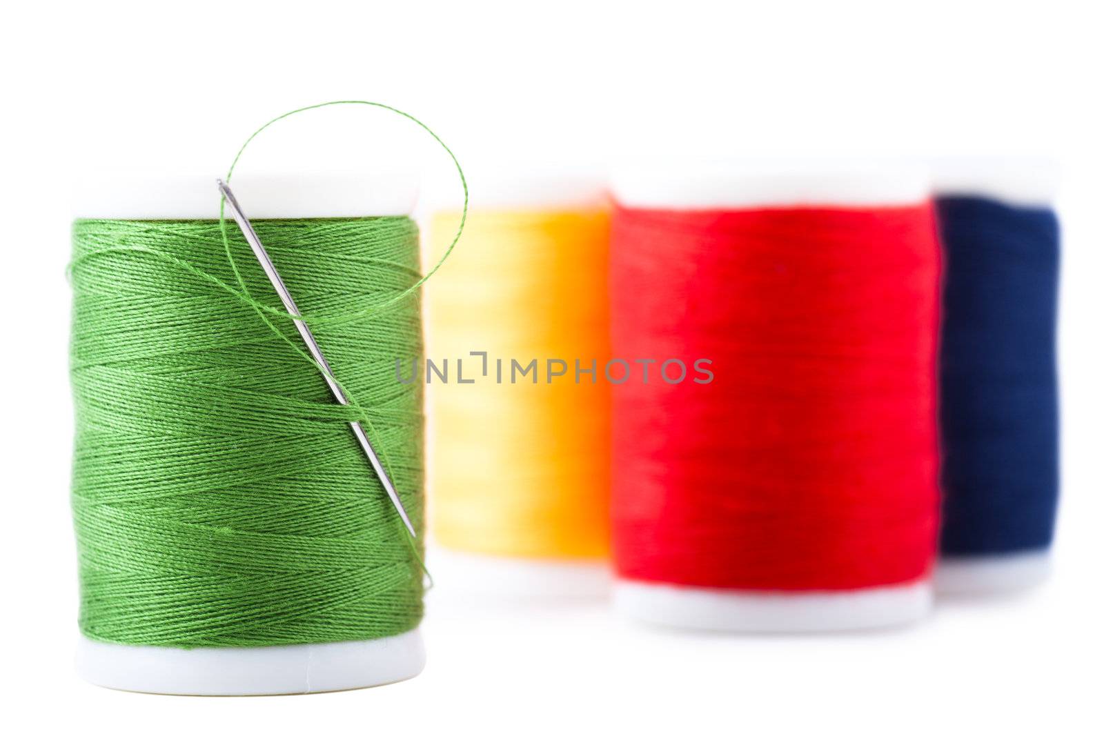 Four spools with green, red, blue and yellow thread and needle