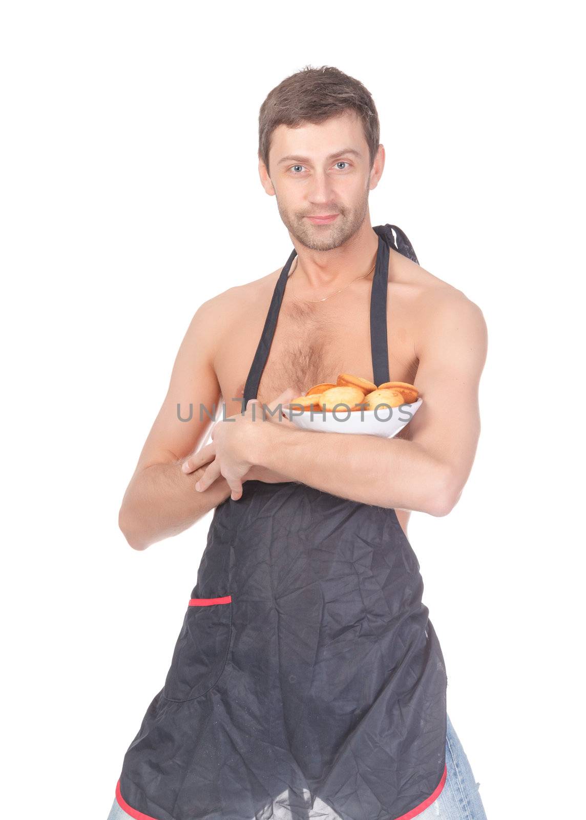 Attractive man trying his hand at baking wearing an apron and carrying a bowl of freshly baked cookies isolated on white