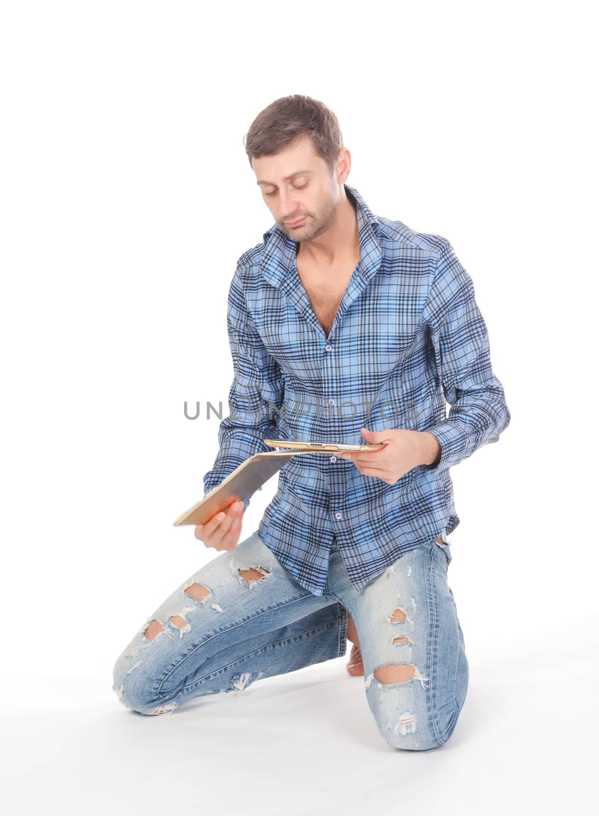 Casual mature man in ragged jeans kneeling barefoot on the floor reading from a tablet pad which he is hand holding