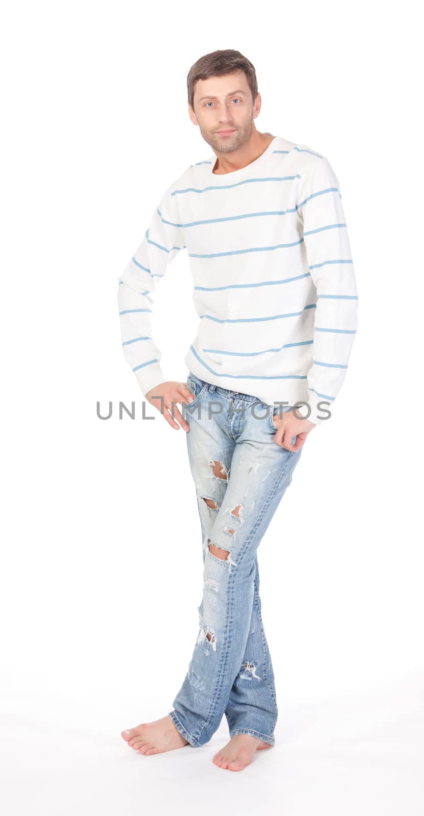 Handsome casual man standing barefoot in trendy ragged jeans with his hands in his pockets over a white background