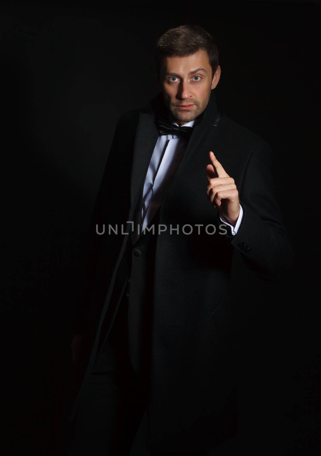 Dramatic portrait of a suave handsome man in a tuxedo and bowtie highlighted in darkness