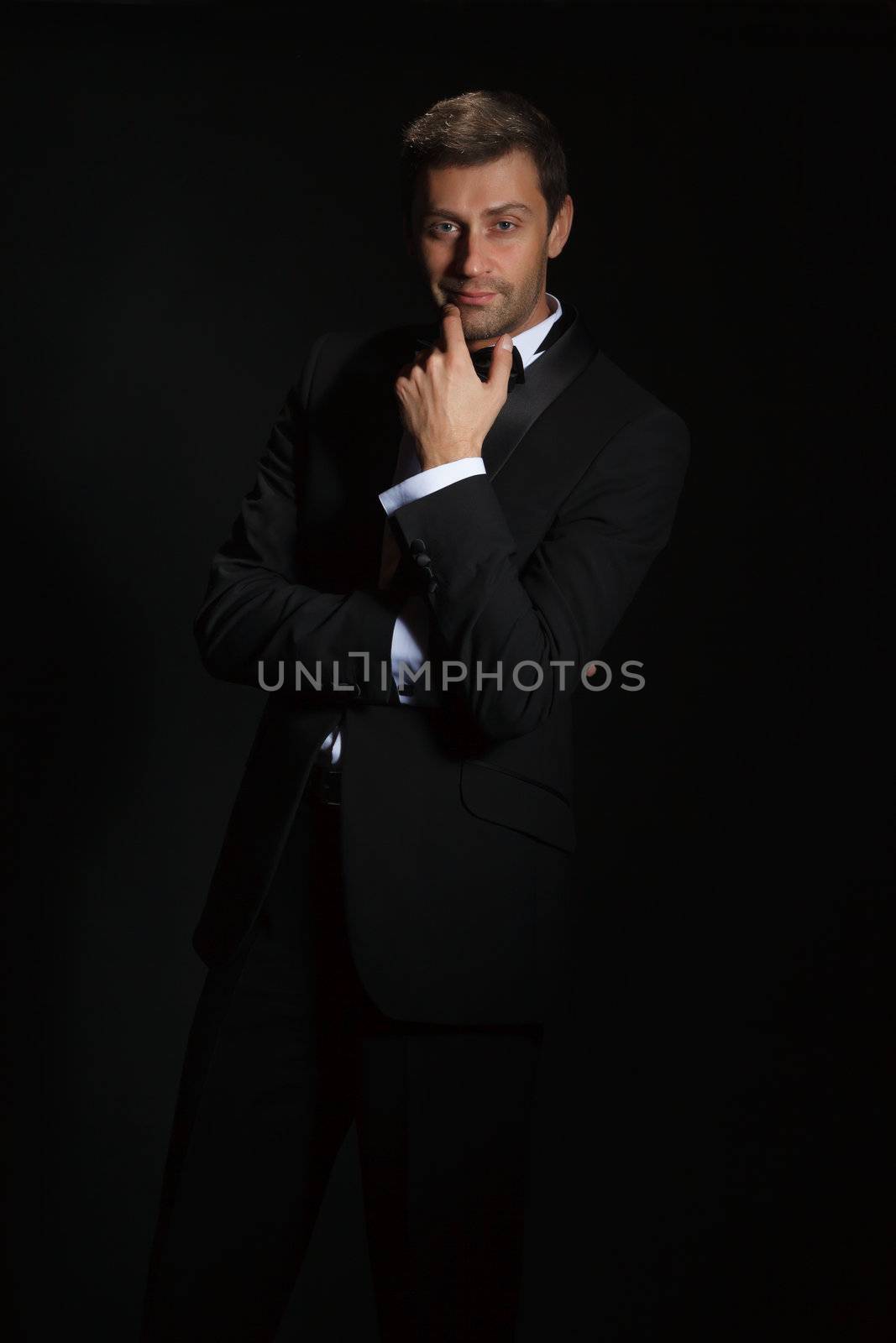 Dramatic portrait of a suave handsome man in a tuxedo and bowtie highlighted in darkness