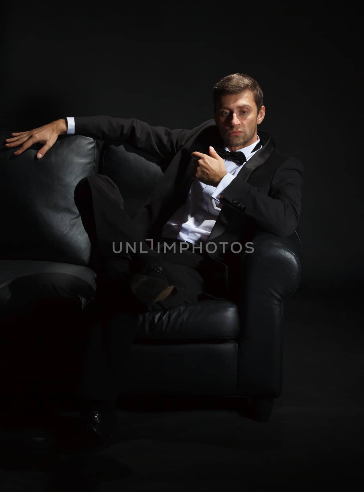 Handsome man in a tuxedo on couch by Discovod