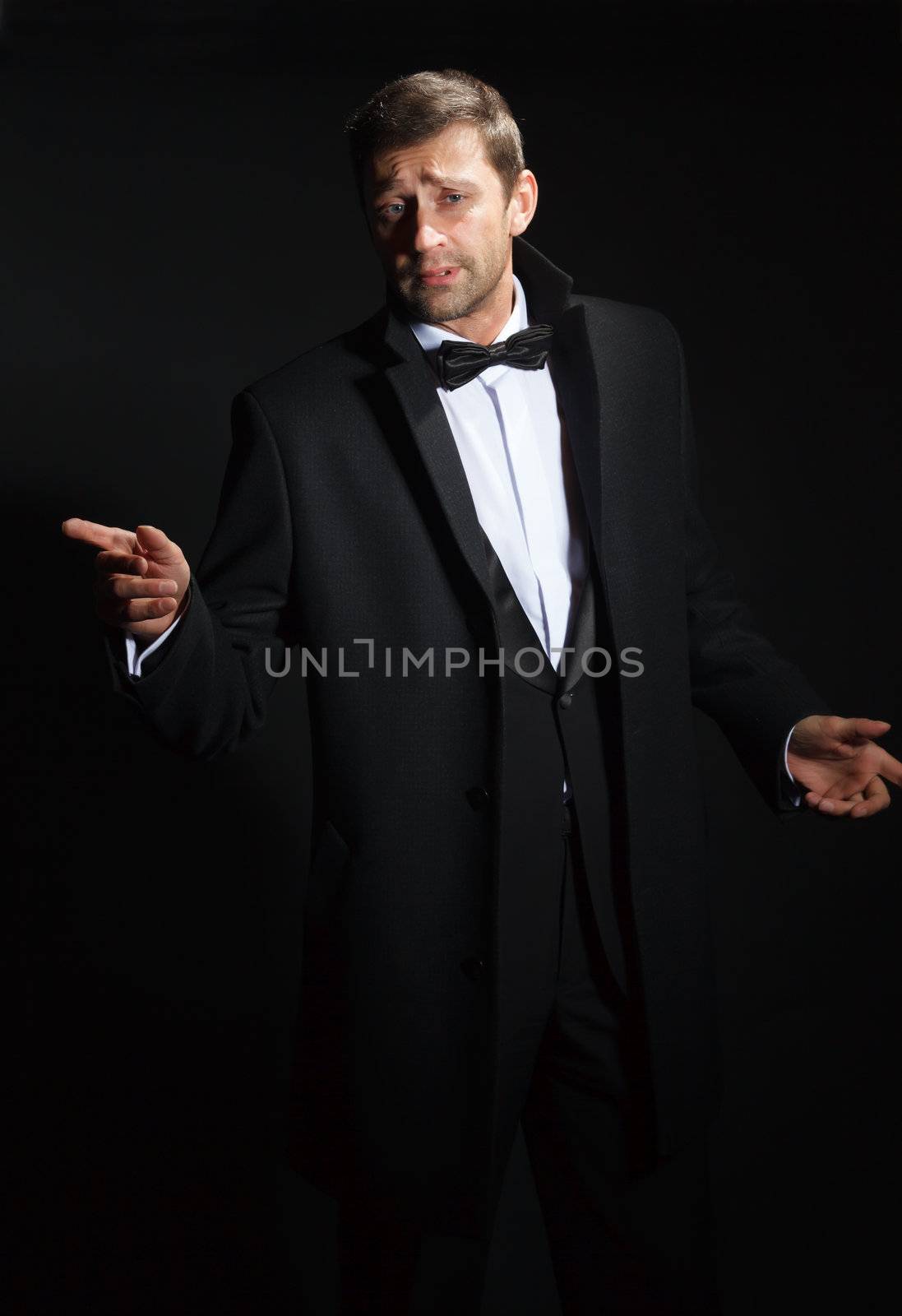 Dramatic portrait of a suave handsome man in a tuxedo and bowtie highlighted in darkness