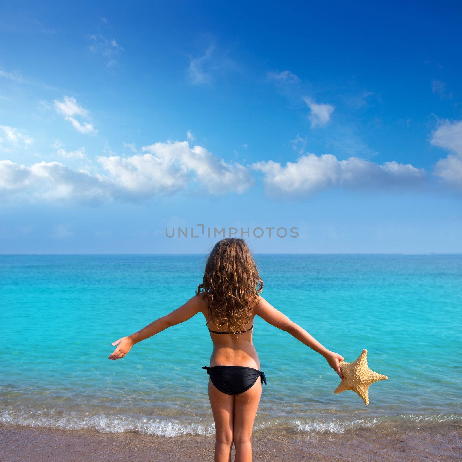 blue beach kid girl with bikini holding starfish looking sea in rear view