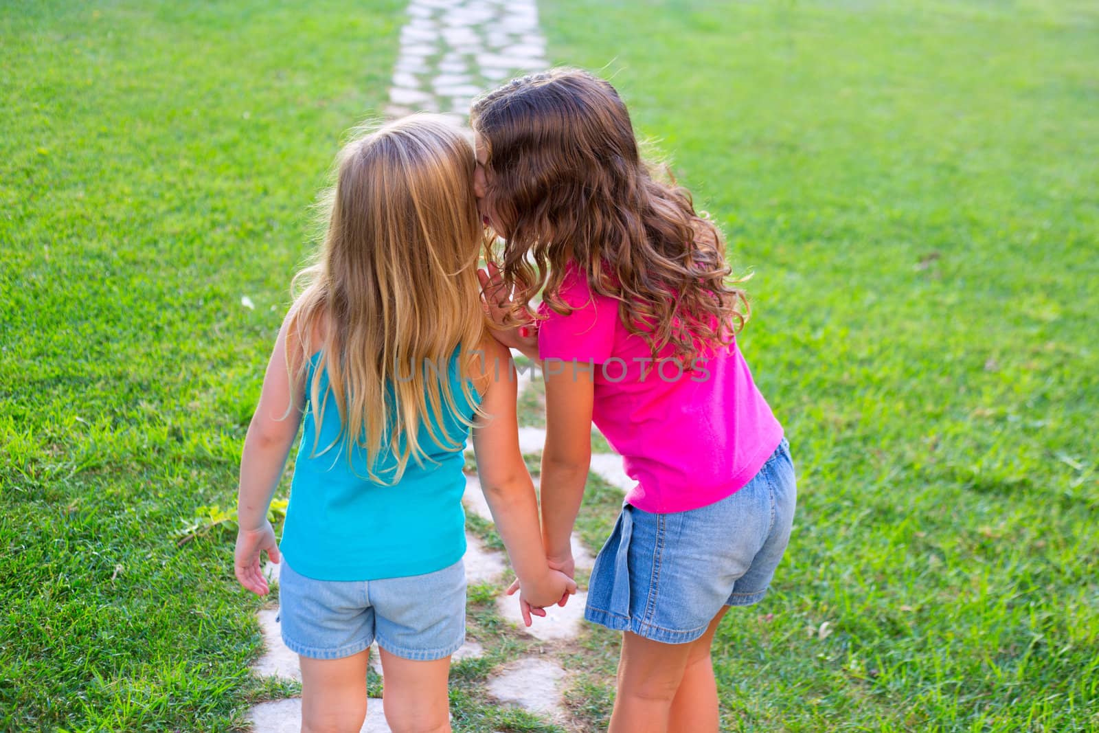 friends sister girls whispering secret in ear in grass garden track park outdoor