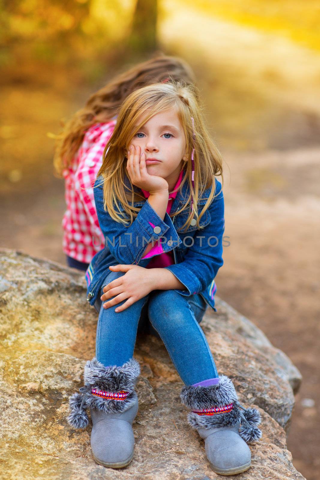 blond kid girl pensive bored expression in the forest outdoor sitting on a rock