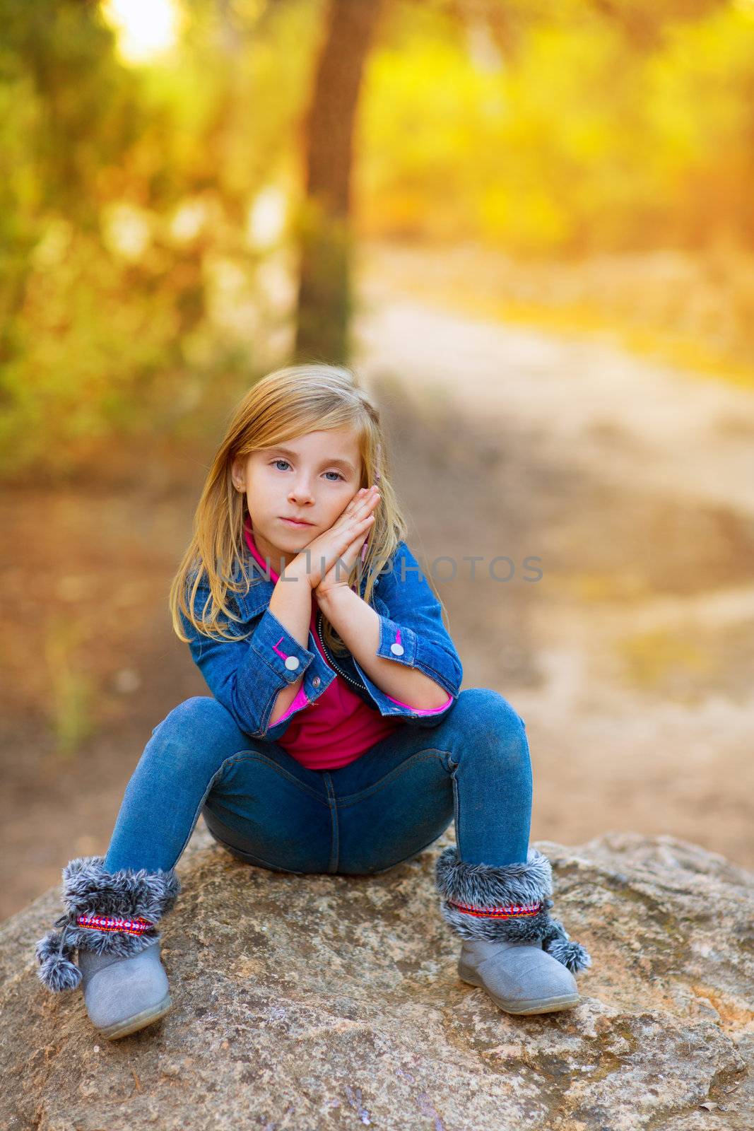 blond kid girl pensive in the forest outdoor sitting on a rock