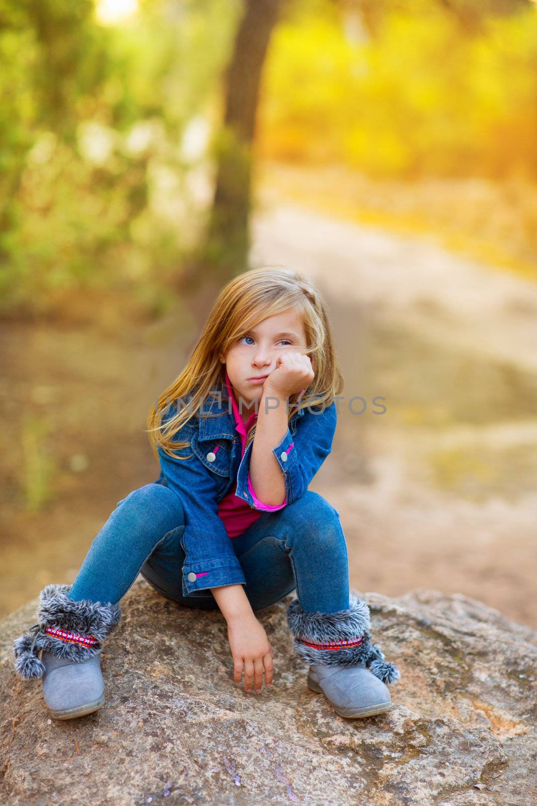 blond kid girl pensive bored expression in the forest outdoor sitting on a rock