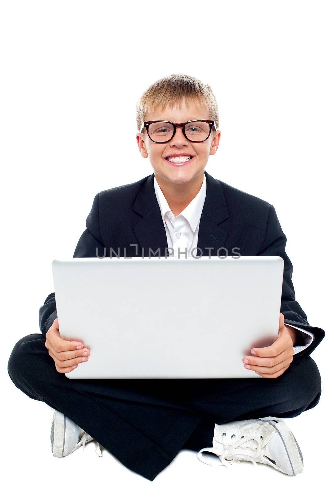 Cheerful young kid sitting on the floor with a laptop. Isolated over white background