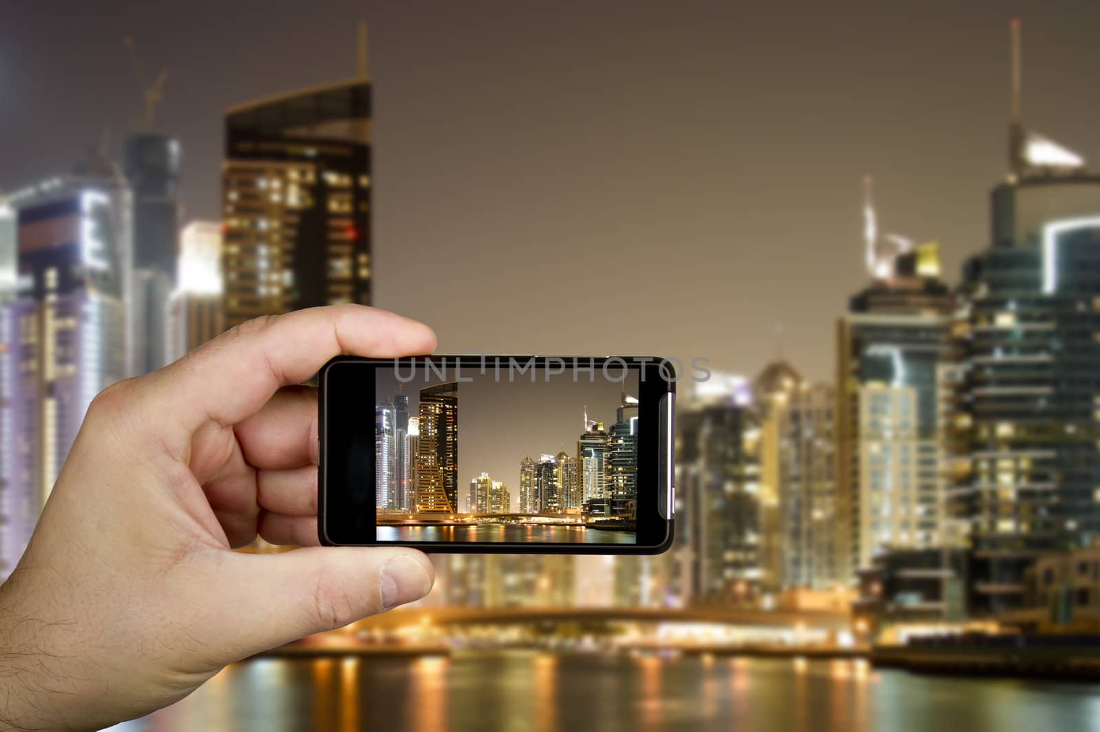 Hand and cellphone with modern buildings in Dubai