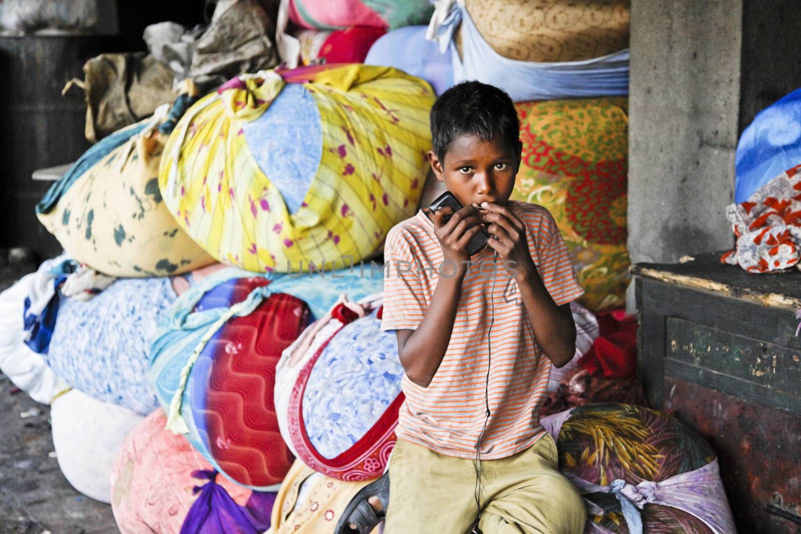 DHOBHI GHAT, MUMBAI, INDIA - FEBRUARY 25, 2012: In the squaller of the commercial hand wash clothes laundry in the heart of Bombay, a boy laborer holds on to his mobile cell phone looking straight into camera lens