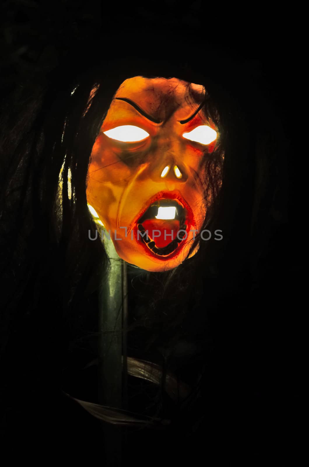 Halloween zombie mask on a stick and shot against black background