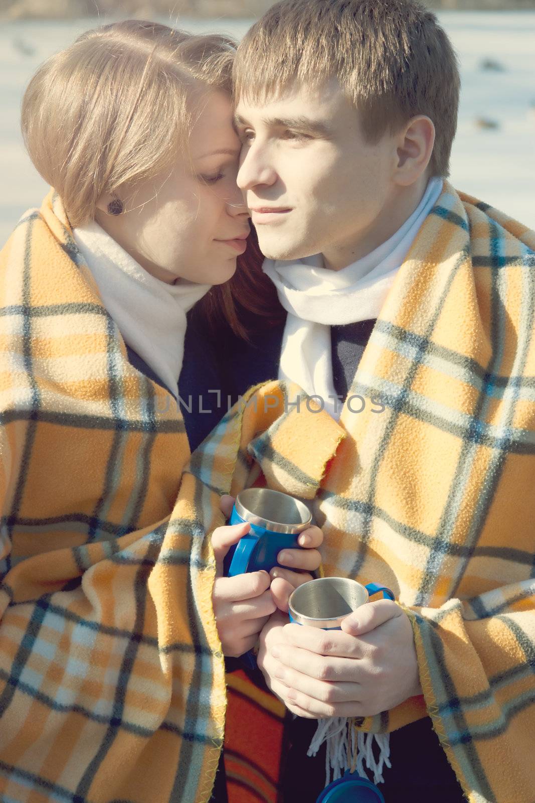 A young couple in love in winter wrapped in a yellow blanket and drink tea