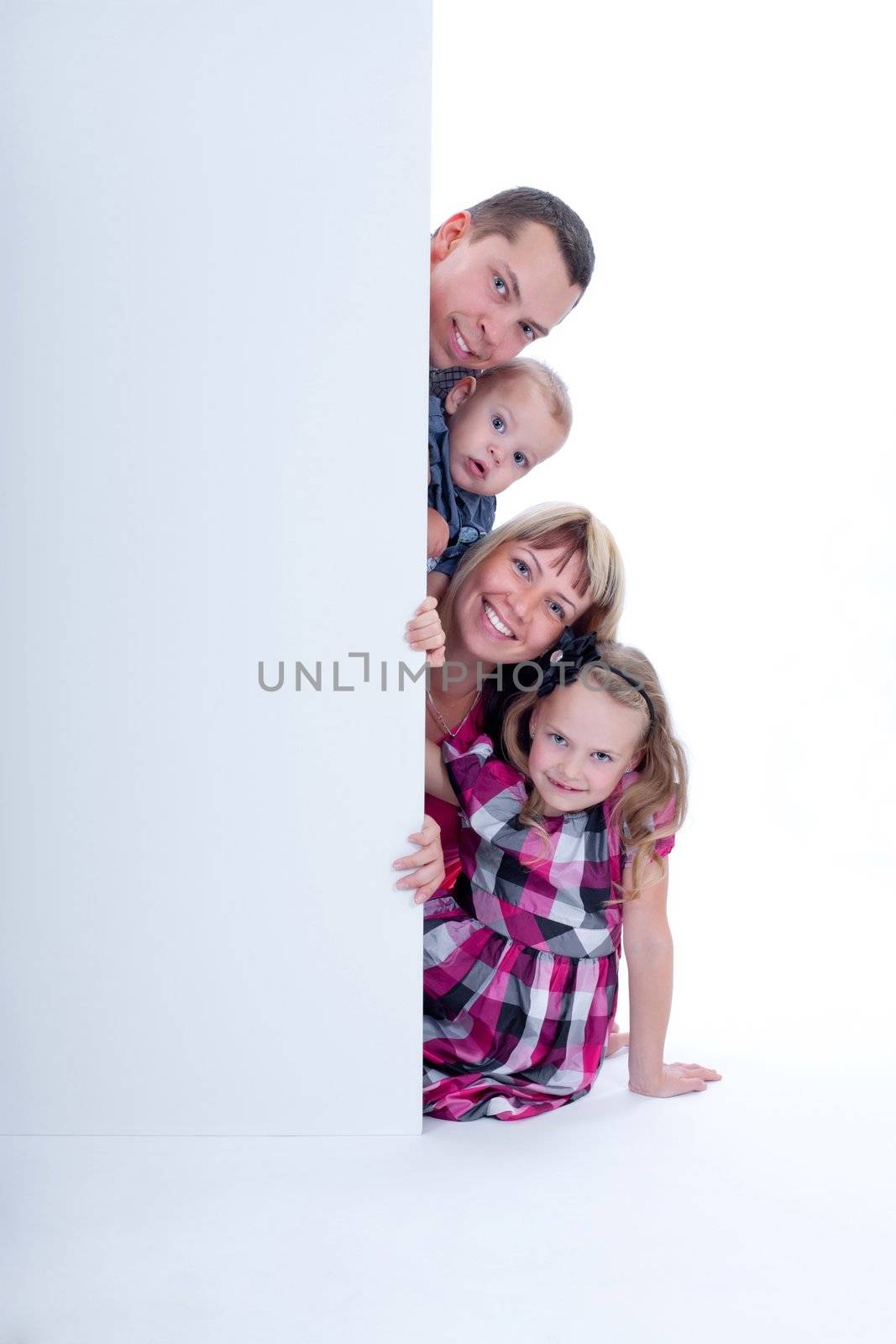 Happy smiling family looking out from behind the wall