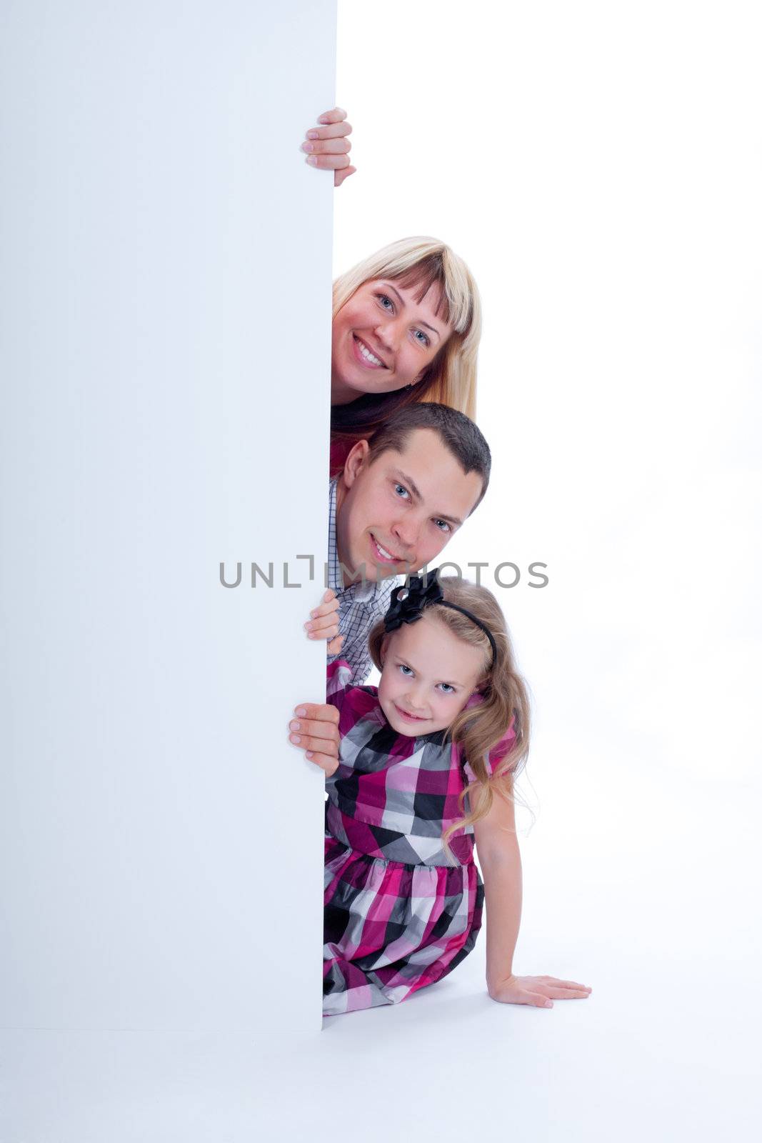 Happy smiling family looking out from behind the wall