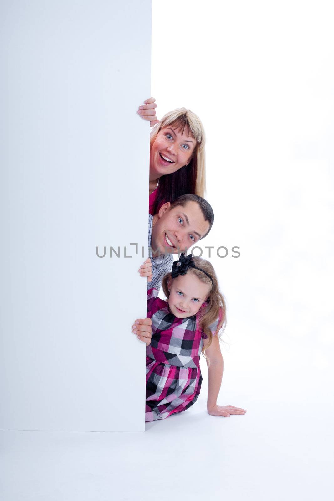 Happy smiling family with amazed facial expressions looking out from behind the wall