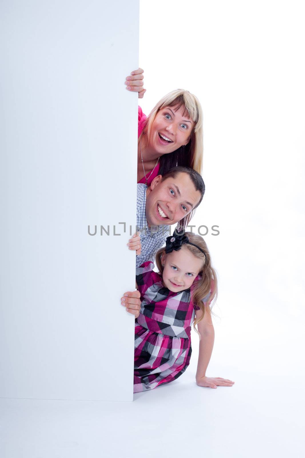 Happy smiling family with amazed facial expressions looking out from behind the wall