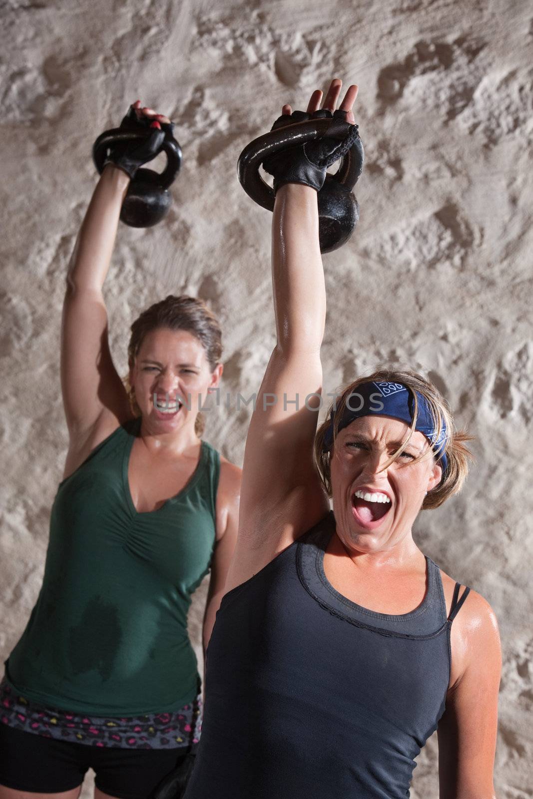Instense women shout as they push kettle bell weights up