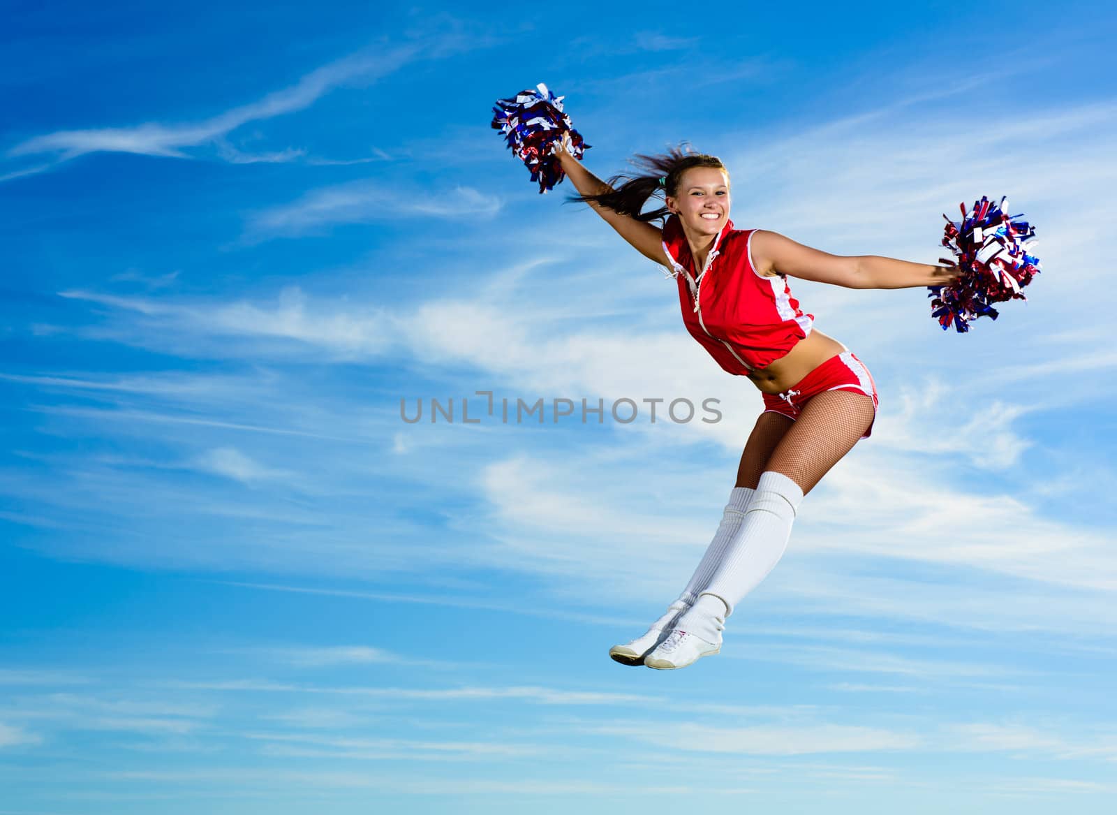 Young cheerleader in red costume jumping against blue sky