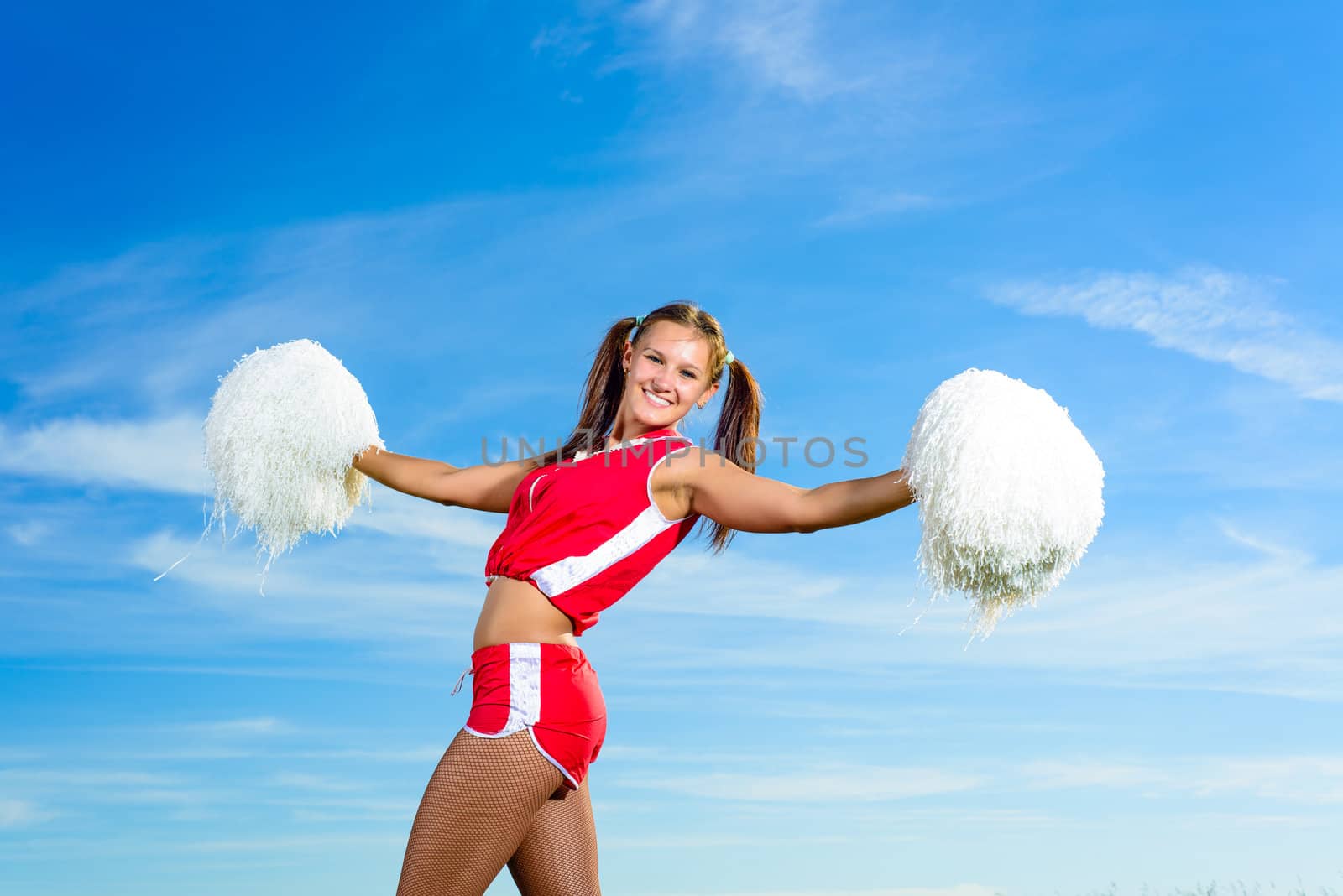 Young cheerleader in red costume with pampon against blue sky