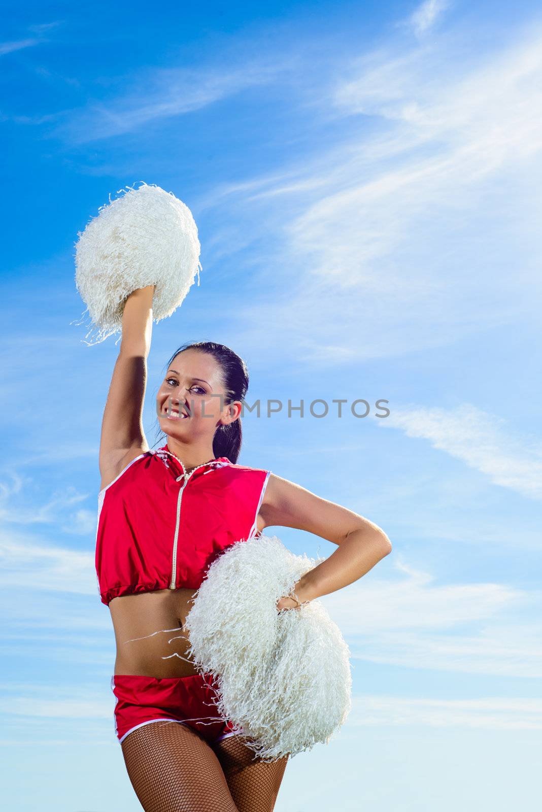 Young cheerleader in red costume with pampon against blue sky