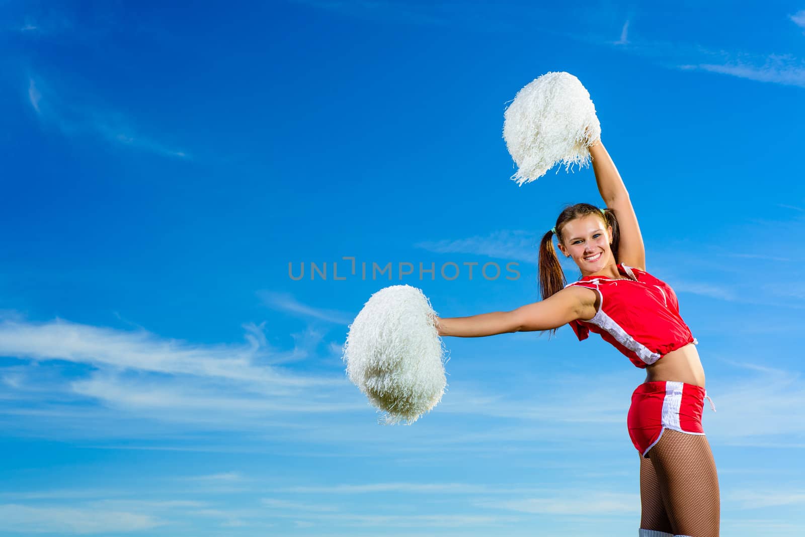 Young cheerleader in red costume with pampon against blue sky