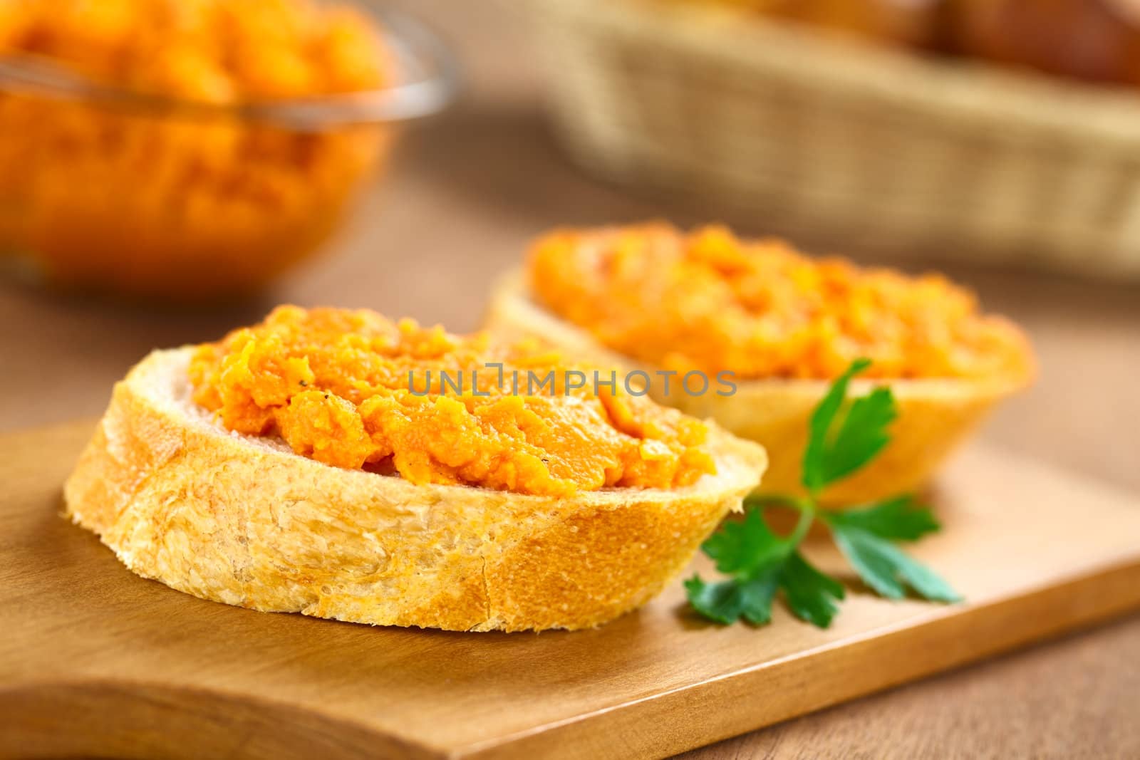 Sweet potato spread on baguette slice on wooden board with bread basket and bowl of sweet potato spread in the back (Selective Focus, Focus on the front of the spread) 