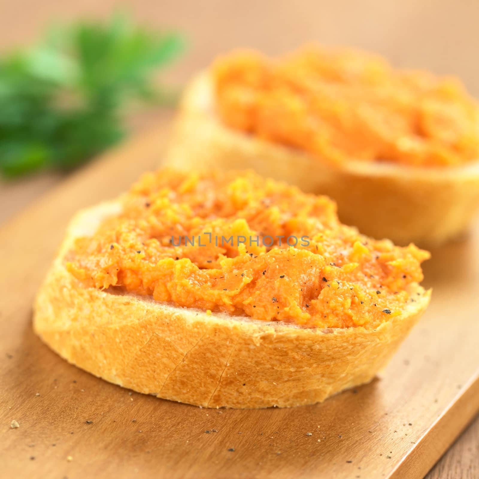 Sweet potato spread on baguette slice with freshly ground pepper on top on wooden board  (Selective Focus, Focus on the front of the spread) 
