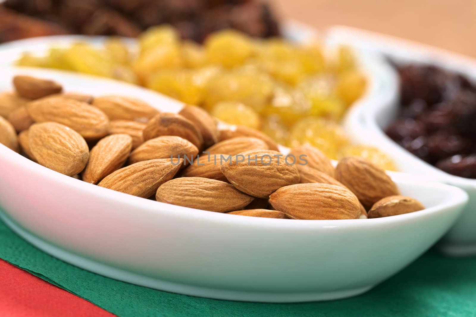 Almonds, sultanas and raisins in small bowls on red and green napkins (Selective Focus, Focus on the almonds in the front)