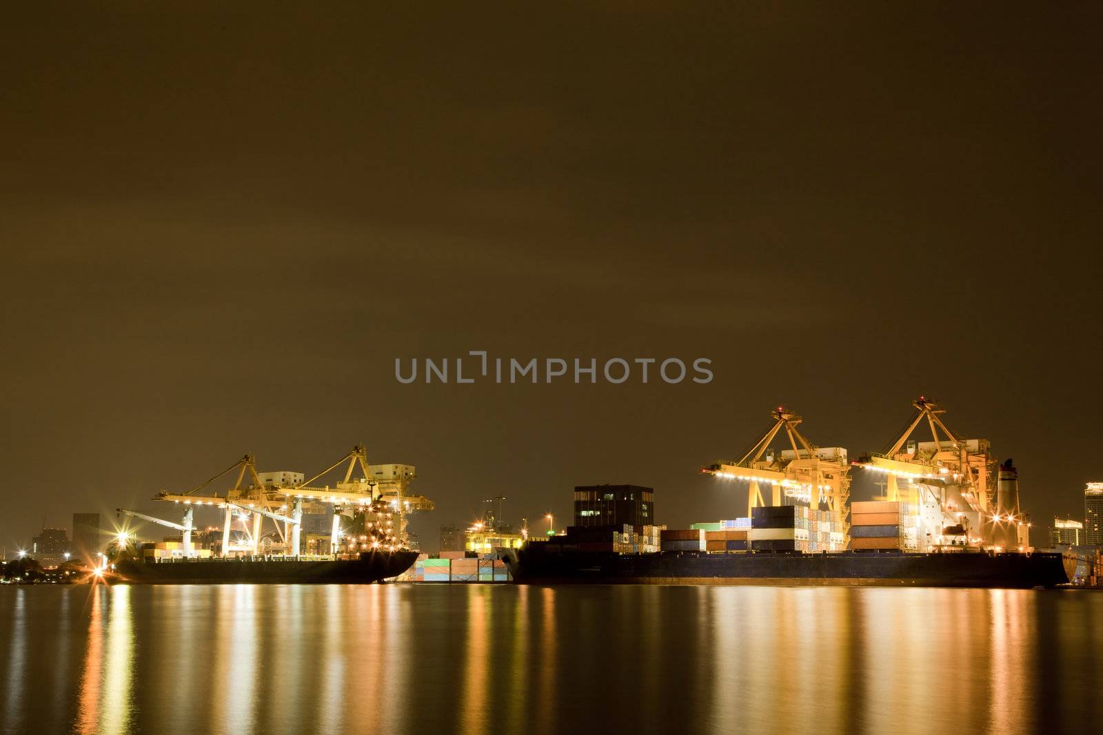 Big Container Cargo freight ship with working crane in shipyard at night for Logistic Import Export background