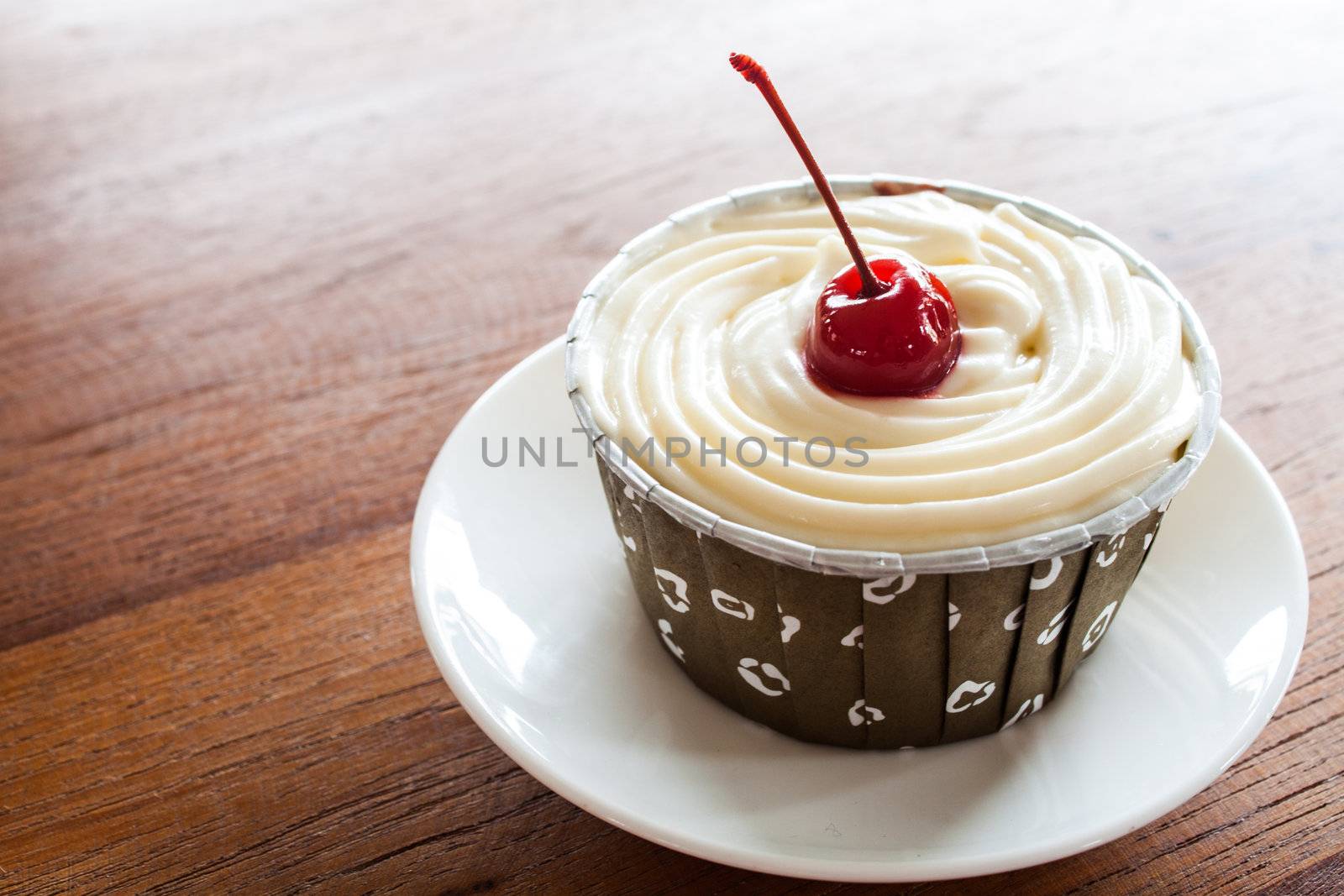 Cupcake with red cherry on white plate