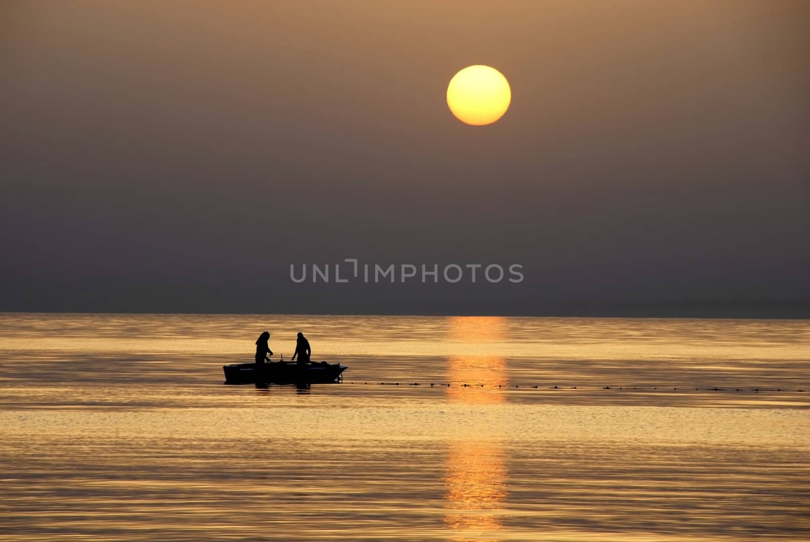 silhouettes of two fishermen fishing in boat on sea at gorgeous sunrise in Tunisia