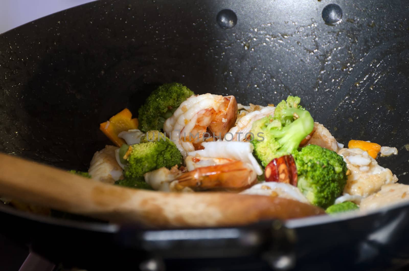 Close-up of shrimps and vegetables in wok with wooden spoon