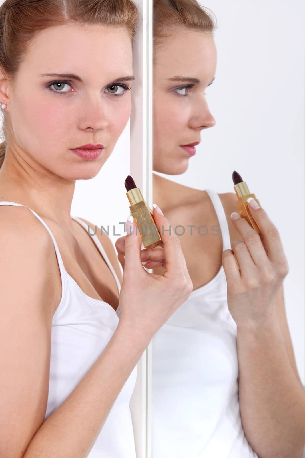 Young woman applying lipstick in a mirror by phovoir