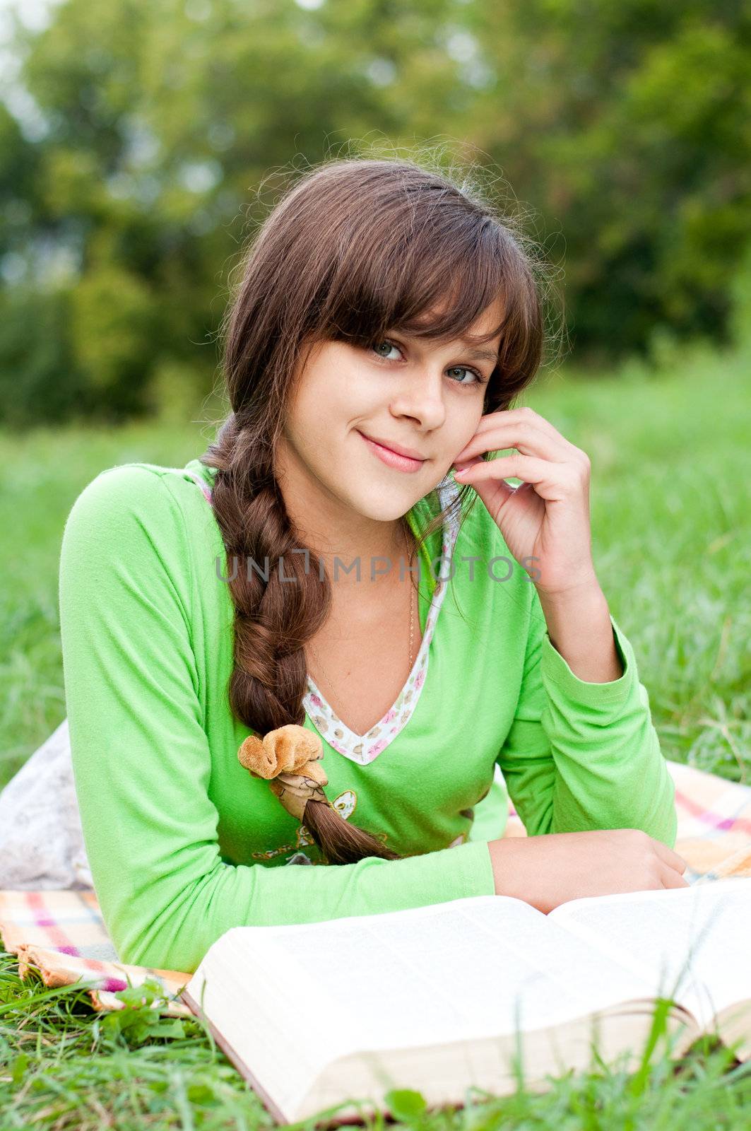 Girl reading a book lying on the grass by olgavolodina