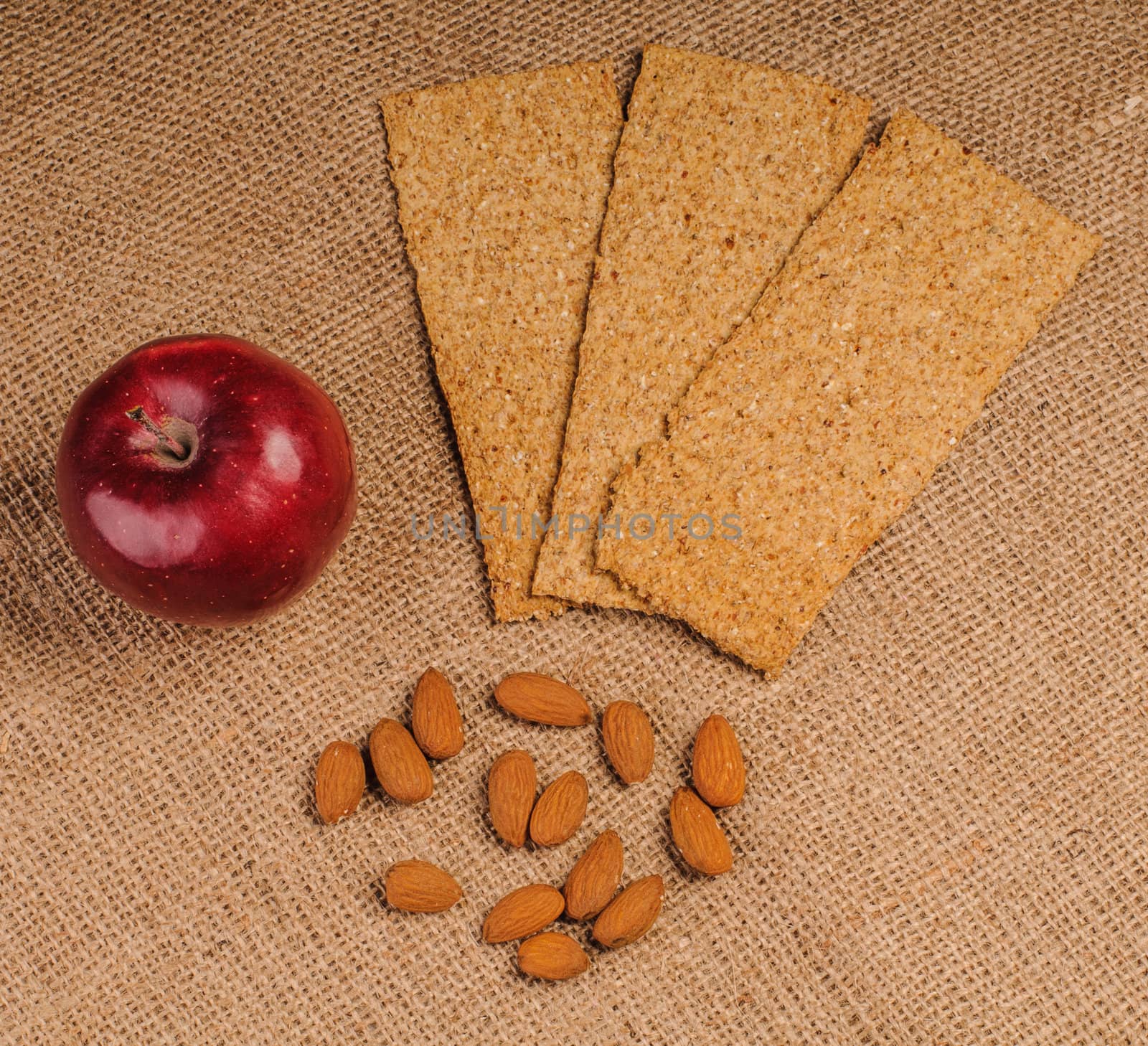 Red apple with crispbread and almonds on sacking background