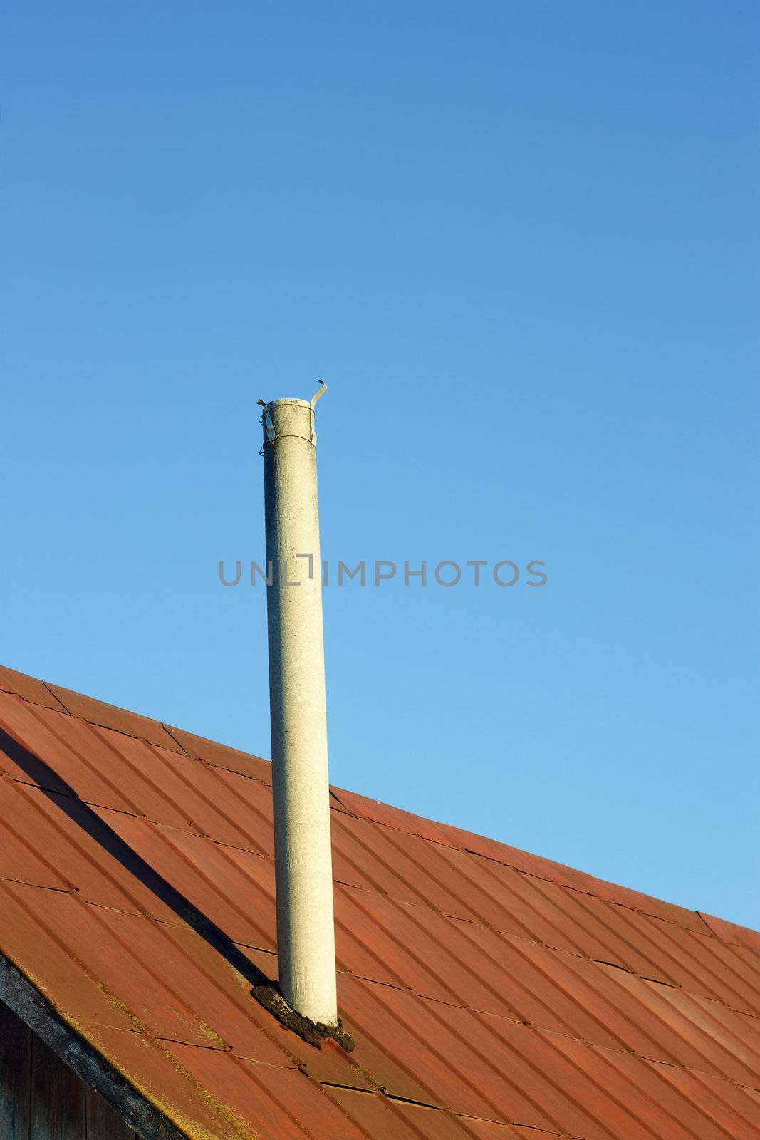 Chimney on an old tinny roof against the blue sky