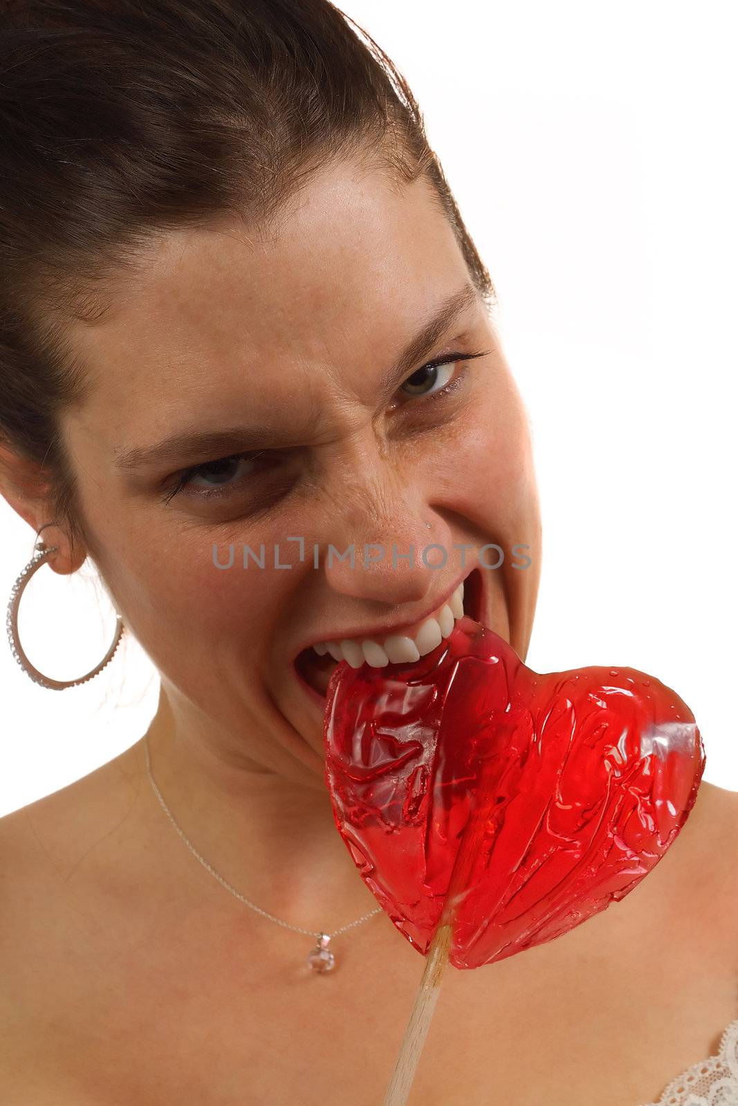 Young woman bites hard on heart shaped lollipop, isolated over white