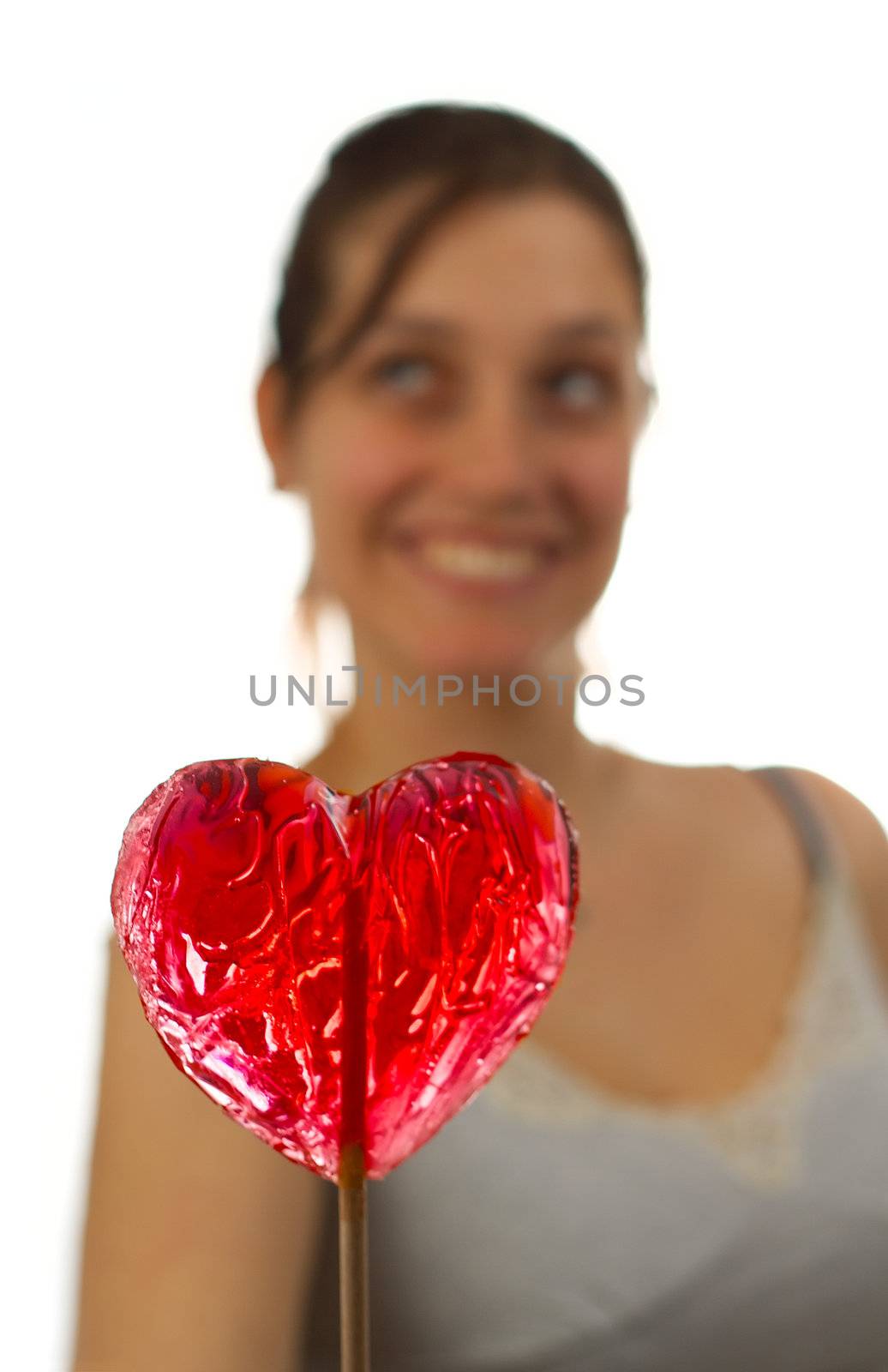 Happy young woman behind heart shaped lollipop, isolated over white
