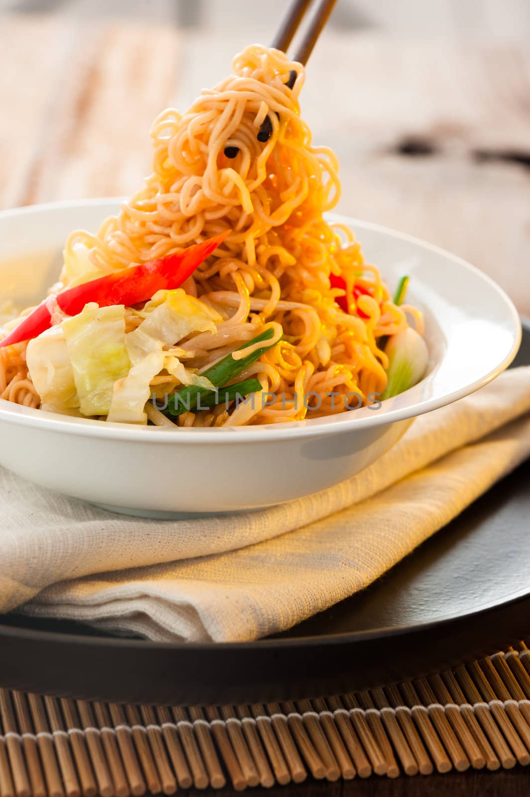 Asian vegetables noodles in white plate and chopsticks on wooden table as background