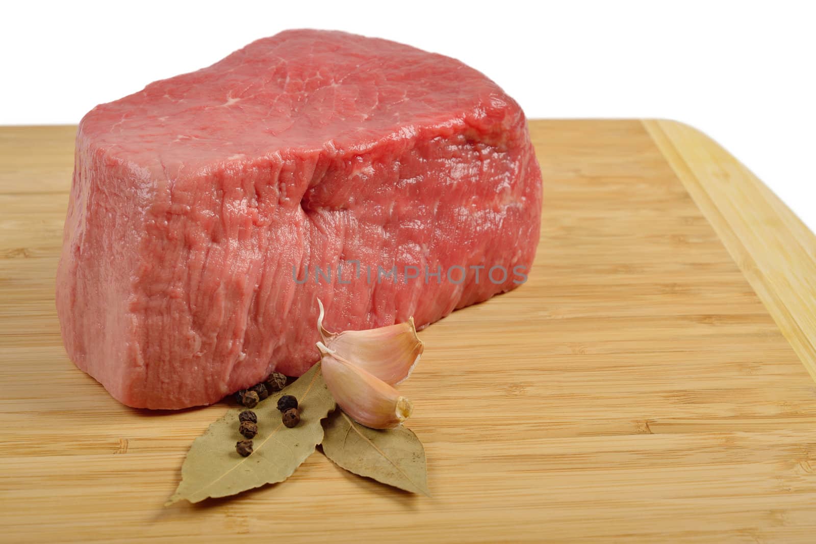 Piece of raw beef on a wooden board, decorated with garlic and bay leaves.