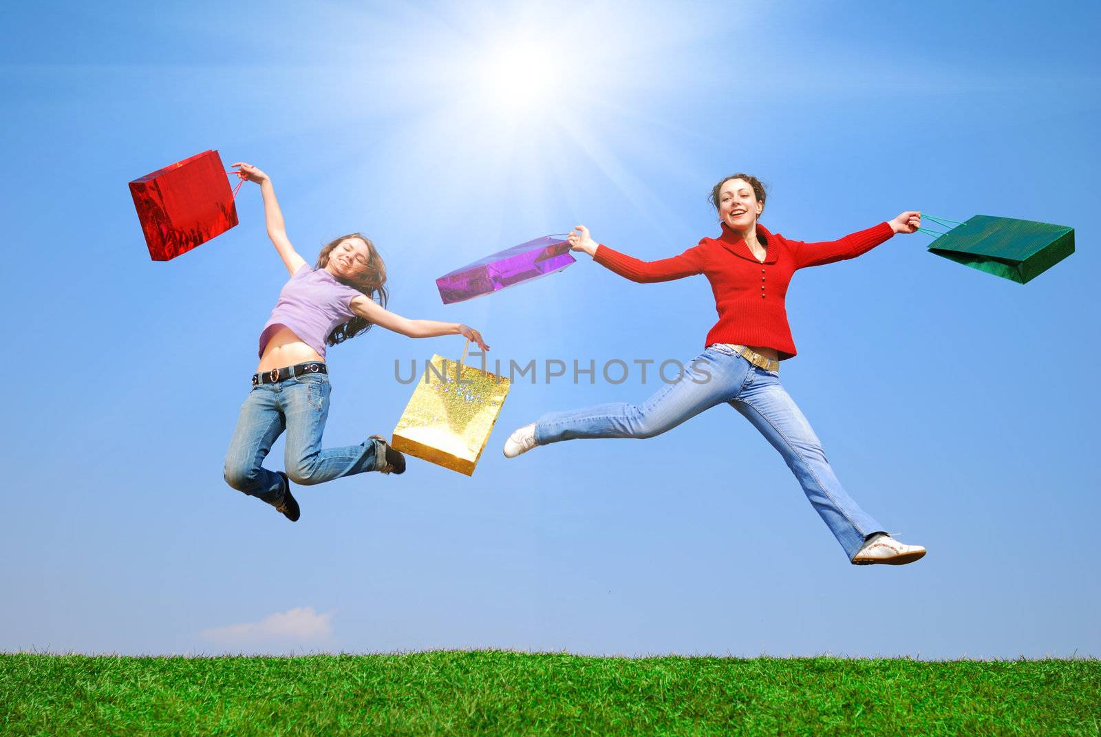 Girls jumping with bags against blue sky