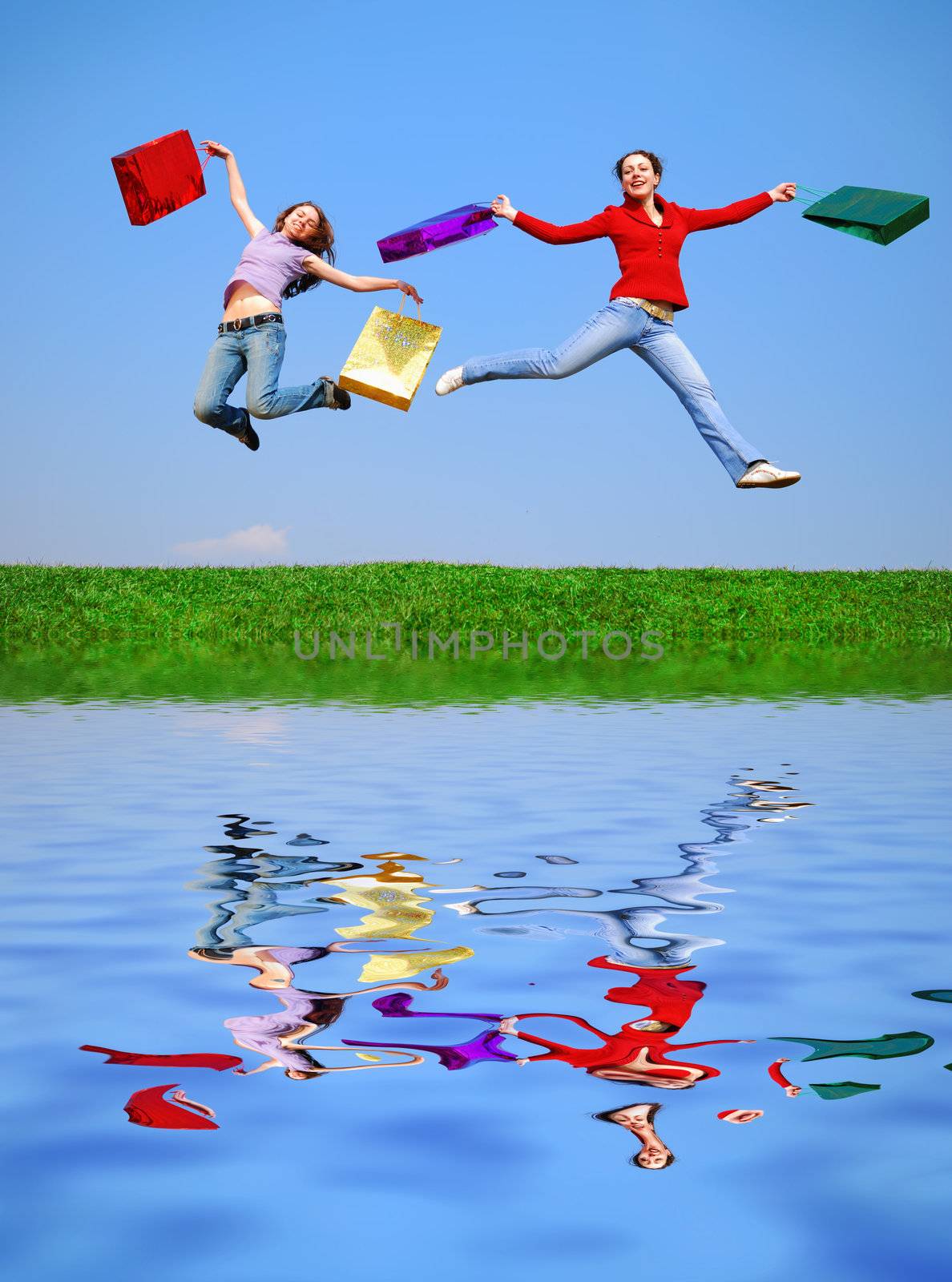 Girls jumping with bags against blue sky with reflection on water