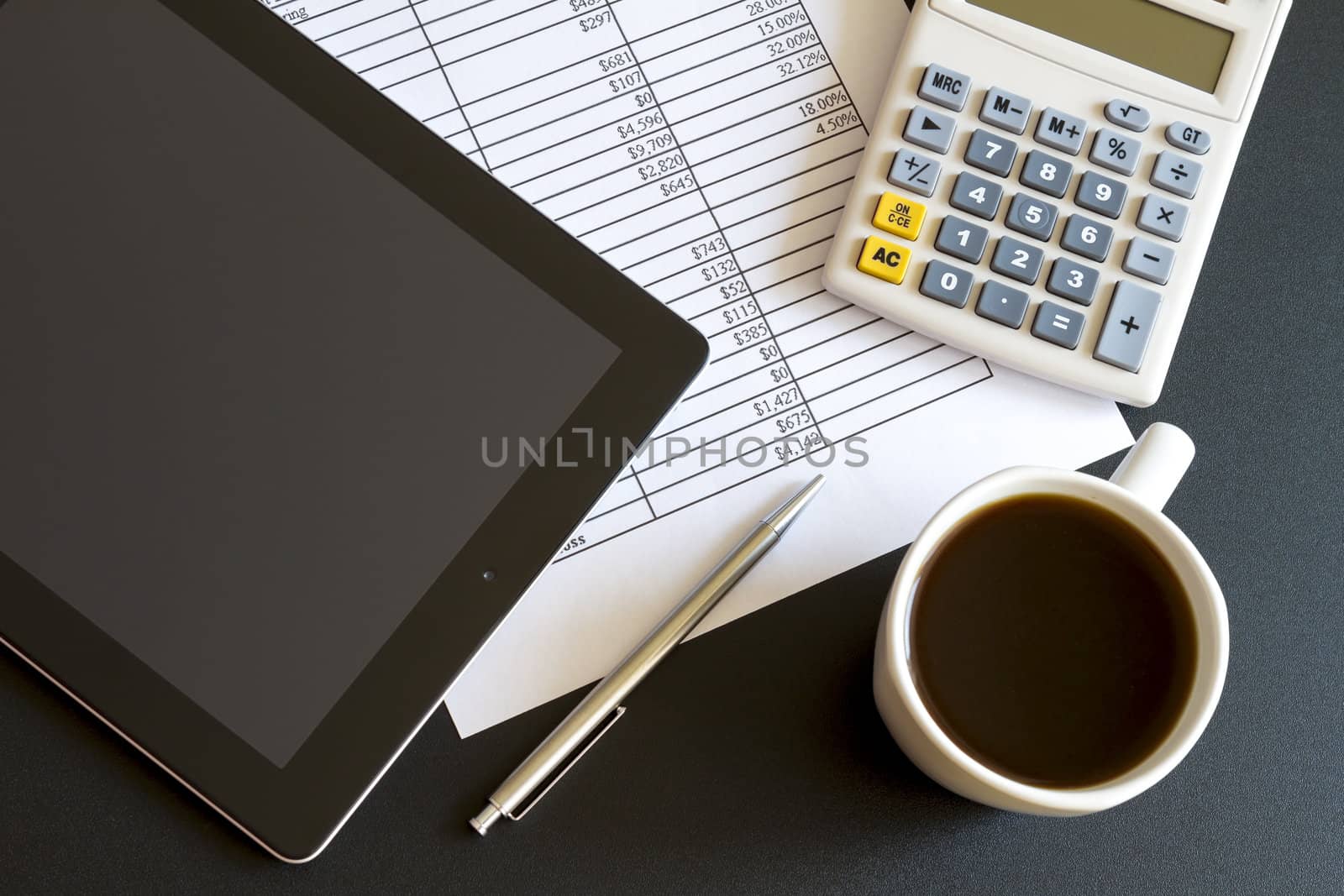 Modern workplace with digital tablet showing charts and diagram on screen, coffee, pen and paper with numbers.