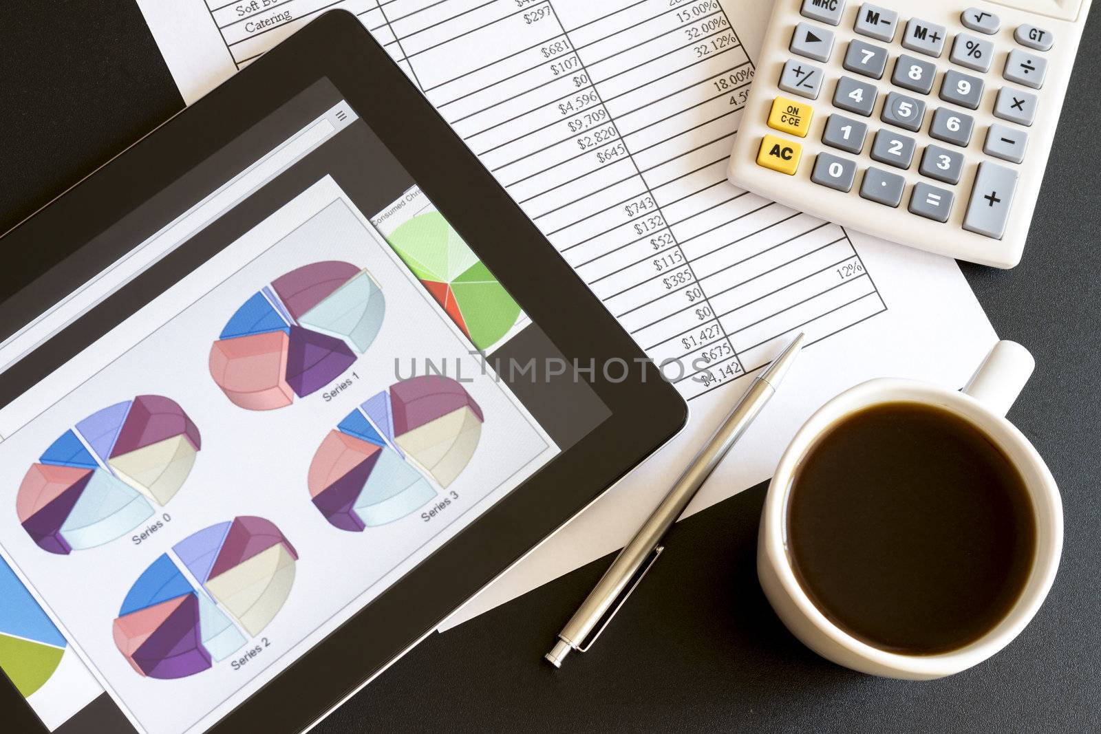 Modern workplace with digital tablet showing charts and diagram on screen, coffee, pen and paper with numbers.