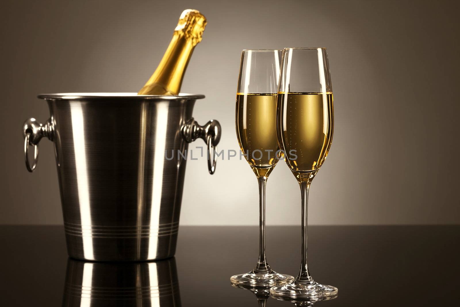 two glasses of champagne with a champagne bottle in a bucket on a mirror with spot light