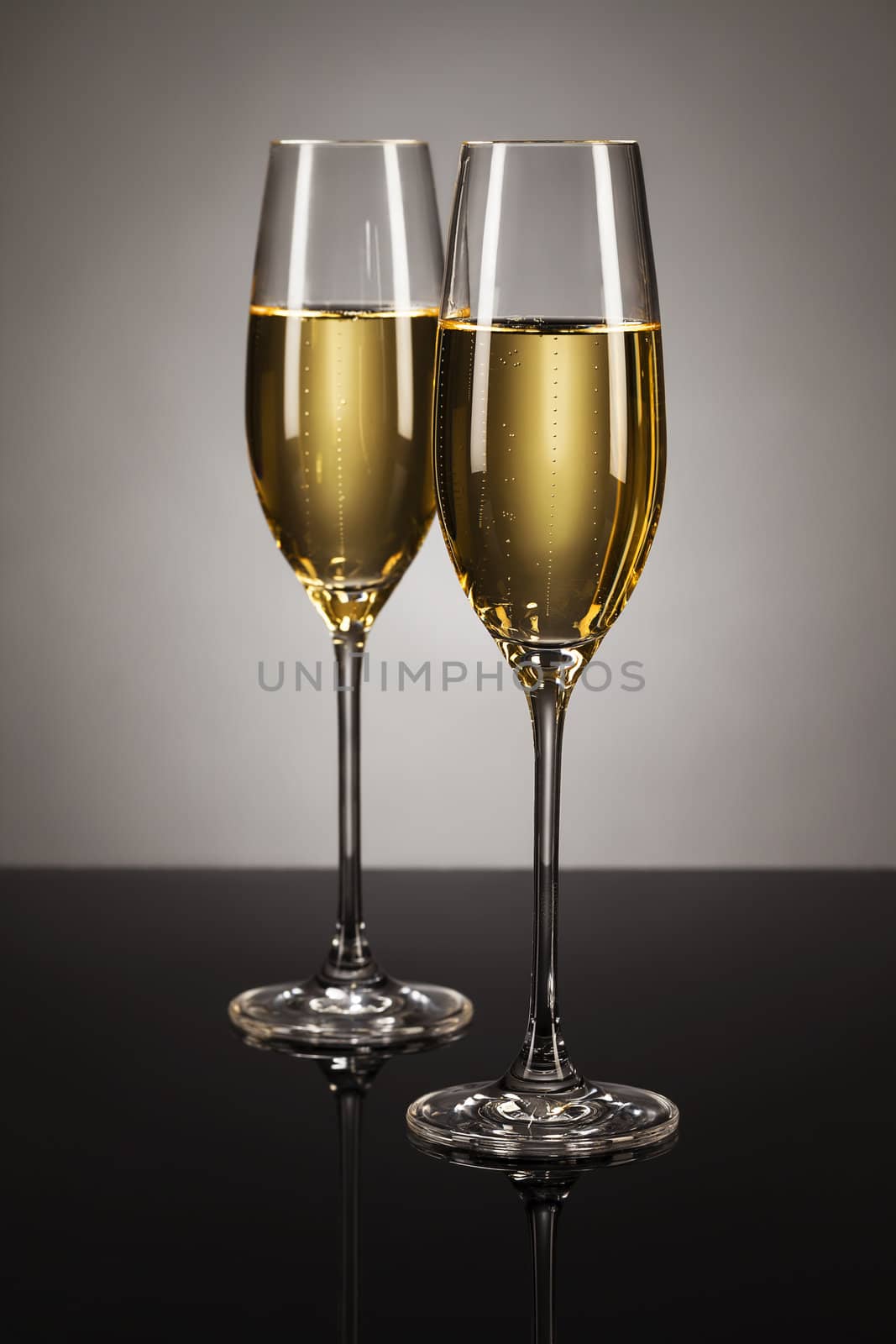 two glasses of champagne on a mirror with a spot light background