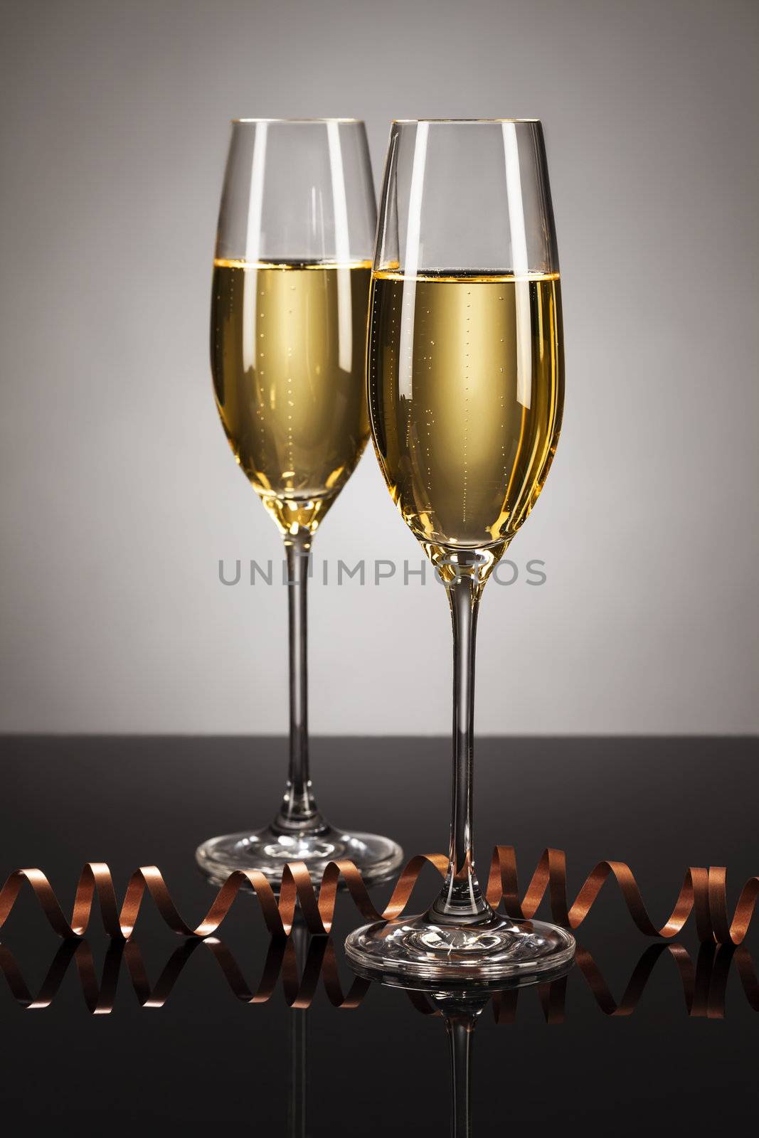 two glasses of champagne with a streamer on a mirror with a spot light background