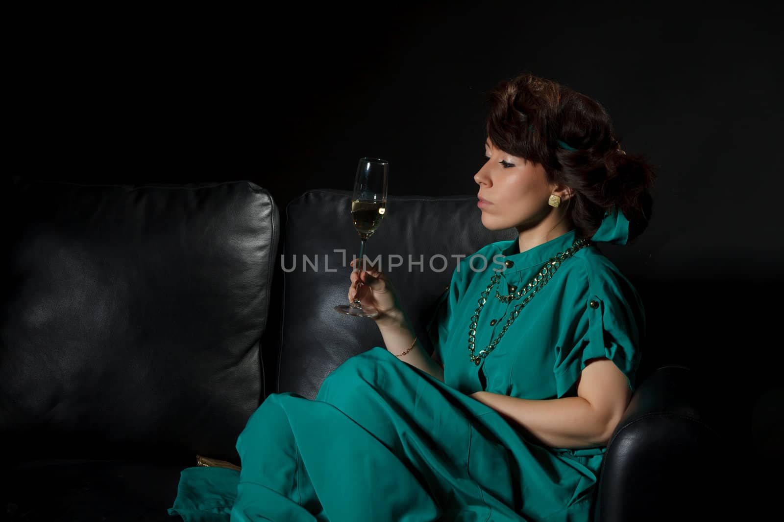 Beautiful girl sitting on a sofa with glass of wine, black background